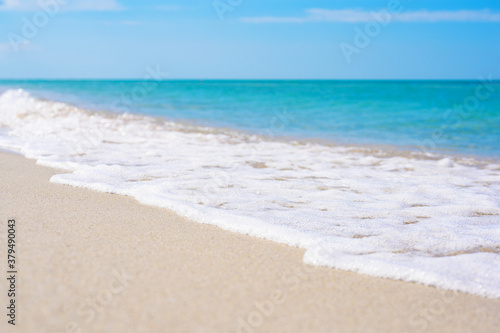 Sea wave on a light sandy shore. The foreground and background are blurred. Calm blue sea in the background.