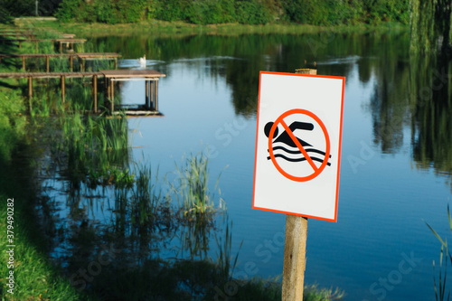 No swimming sign. Entering water is forbidden. Safety lake shore restrictions. Shallow water danger background. Small forest fishing pond.