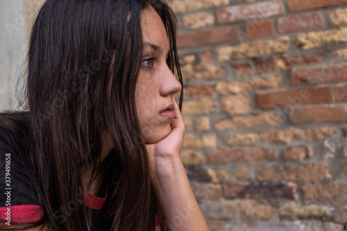 Long haired teenage girl with hand on chin looking away, side view.