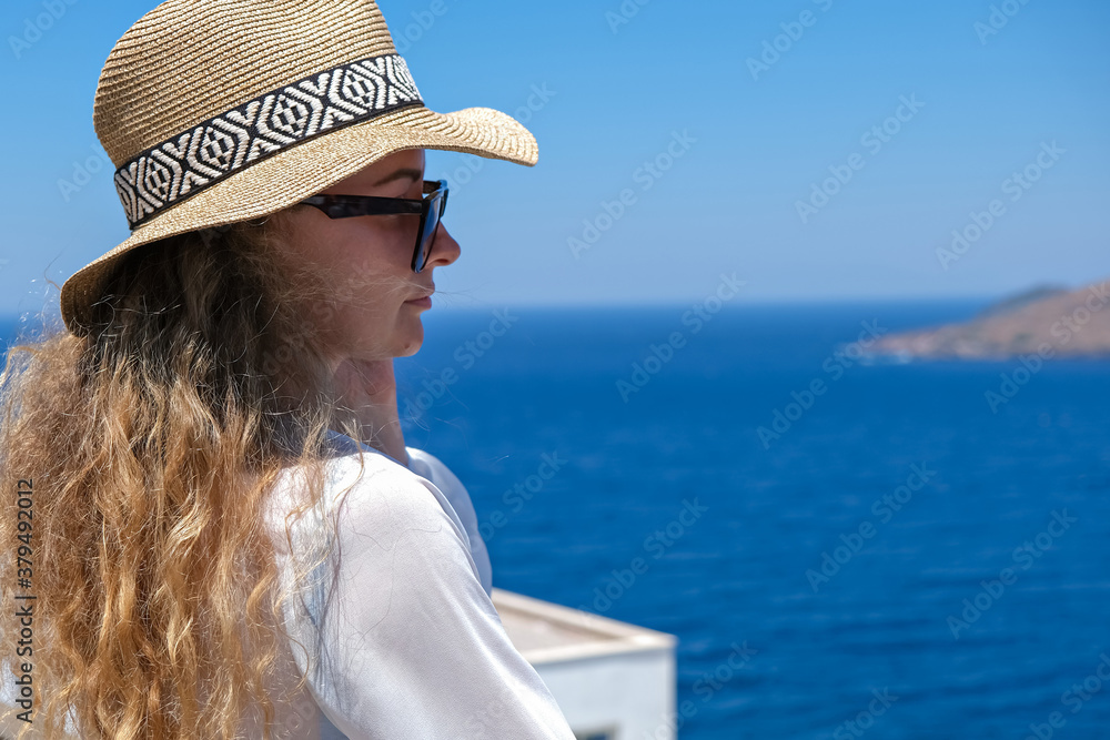 Beautiful young woman in white dress sunglasses and bikini straw hat looking at sea view in resort hotel villa
