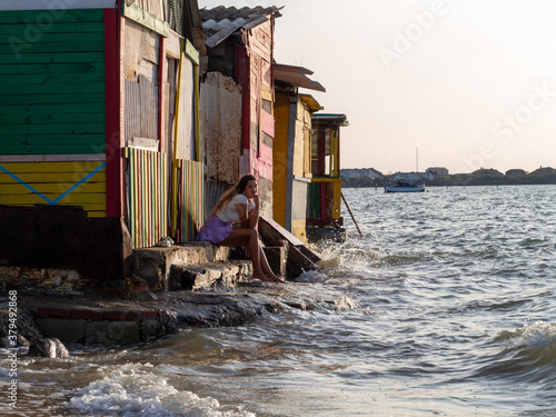 Mujer joven sentada en unas casas de colores en el mar durante la puesta de sol