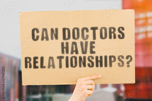 The question " Can doctors have relationships? " on a banner in men's hand with blurred background. Relationship. Couple. Love. Clinic. Profession. Hospital. Communication. Job