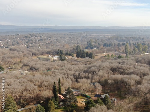 Vista aérea de un valle con algunas casas de veraneo rodeadas de árboles y montañas al fondo. 