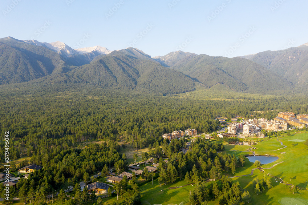 Aerial view from drone. Stunning view of mountains and hotels of mountain resort Bansko in morning at dawn. Beautiful landscape of sunrise in mountains is shot from drone. Travel and vacation concept.