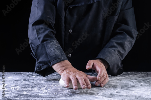 Chef making dough for pizza on dark backrground