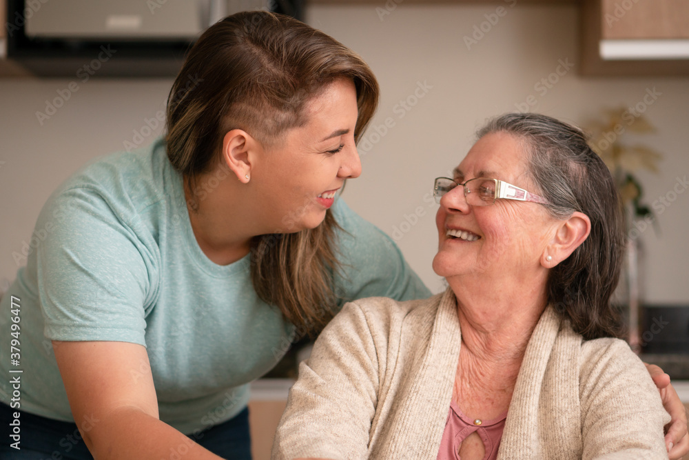 Portrait of latin grandmother and granddaughter looking to each other at kitchen table, inside. Relationship, leisure, domestic life, family concept.. Portrait of latin grandmother and granddaughter looking to each other at kitchen table, inside. Relationship, leisure, domestic life, family concept..