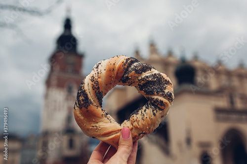 Tourists holding bagel obwarzanek traditional polish cuisine snack on Market square in Krakow. Travel Europe