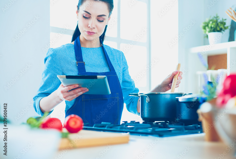 Young woman using a tablet computer to cook in her kitchen Young woman using a tablet computer to cook in her kitchen