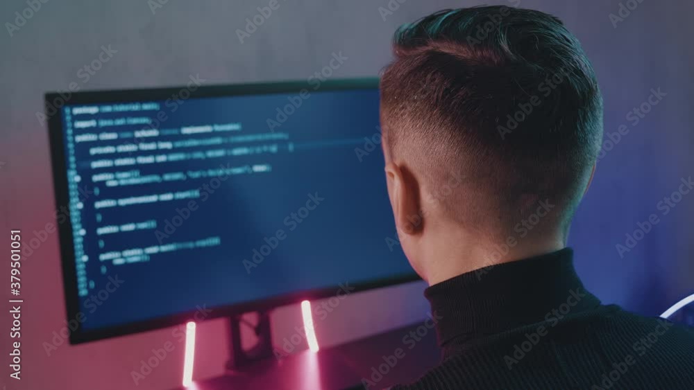 IT Professional Programmer man is typing code. Developer at work at computer. Hacker hacking late at night in neon lights. IT Professional Programmer man is typing code. Developer at work at computer. Hacker hacking late at night in neon lights.