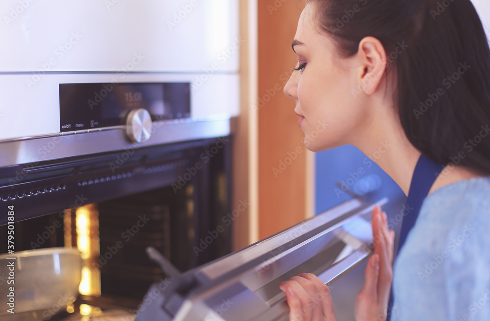 Beautiful young woman checking how her cake is doing in the oven Beautiful young woman checking how her cake is doing in the oven
