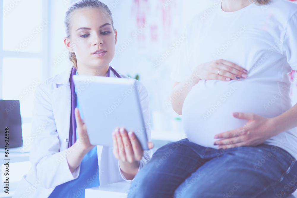 Fototapeta premium Smiling woman doctor shows pictures on the tablet to pregnant young woman at hospital.