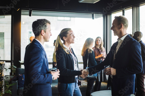 Happy male and female congress shaking hands while standing with colleague in office photo