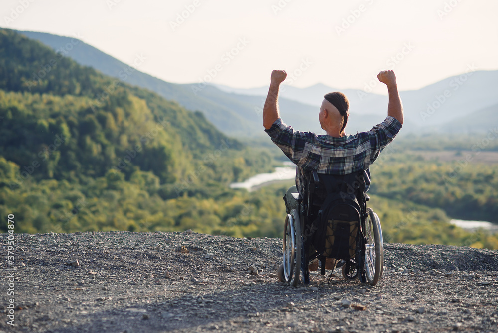 Lonely young man in a wheelchair enjoying fresh air in sunny day on the mountain. People with disabilities travelling. Lonely young man in a wheelchair enjoying fresh air in sunny day on the mountain. People with disabilities travelling.
