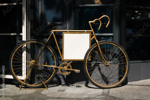 Golden bicycle for decoration of entrance to restaurant with space for logo. White plastic panel mockup, stylish advertising