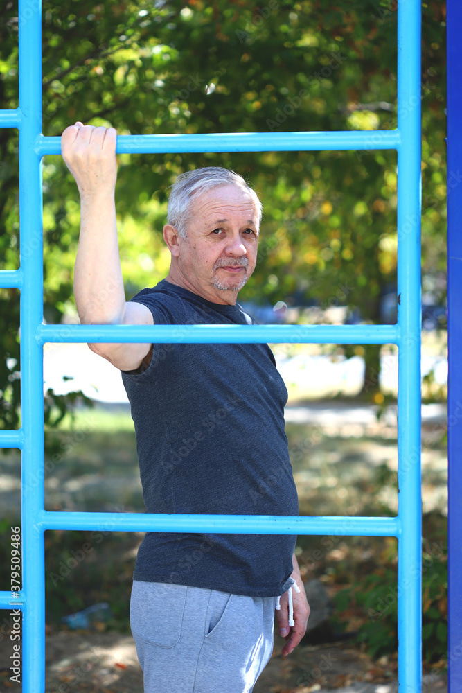 Fototapeta premium Senior man doing exercises in the outdoor gym. The concept of maintaining health at any age. Recovering from a heart attack or stroke. Selective focus. Toning.