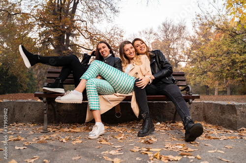 Fun positive girls, posing while sitting on park bench, autumn season