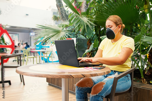 Woman wearing a mask working at her desk looking at the laptop outdoors in a shopping center back to work after the COVID-19 blockade pandemic. photo