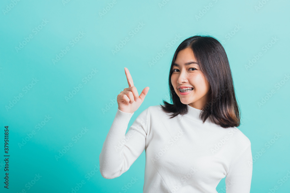 Portrait of Asian teen beautiful young woman smile have dental braces on teeth laughing point finger side away blank copy space, studio shot isolated on blue background, medicine and dentistry concept Portrait of Asian teen beautiful young woman smile have dental braces on teeth laughing point finger side away blank copy space, studio shot isolated on blue background, medicine and dentistry concept