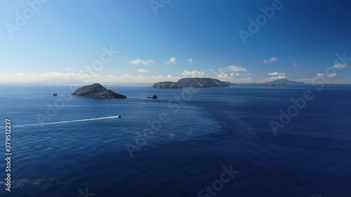 Forwards aerial drone flight over ocean towards islands with single boat on clear day sky photo