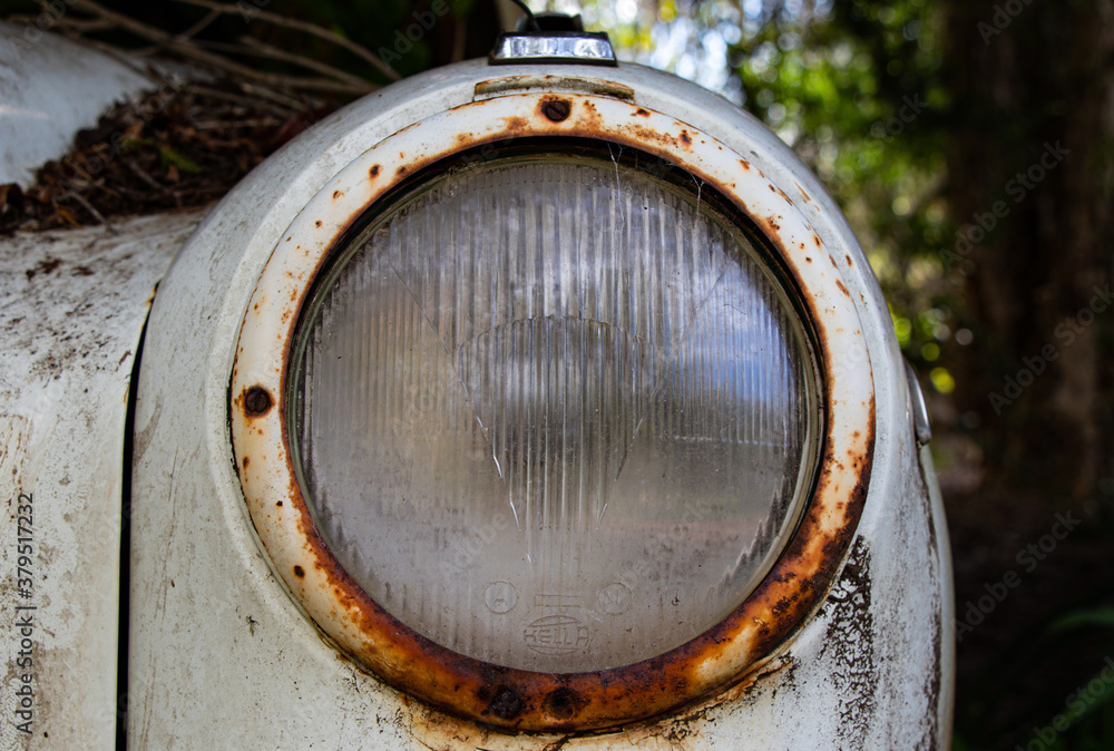 Antique glass Hella car headlight on a rusted car body Antique glass Hella car headlight on a rusted car body