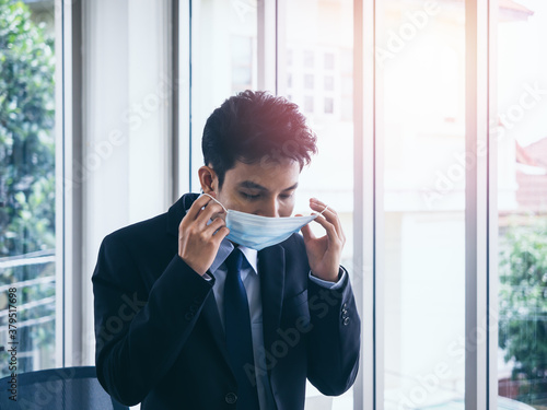 Young Asian businessman in suit wearing medical face mask in office.