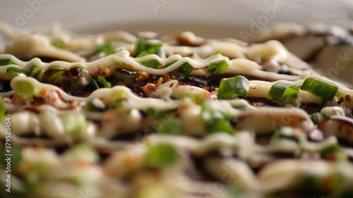 Closeup of the topping of mayonnaise, cream, teriyaki sauce, and spring onions on a okonomiyaki pancake 