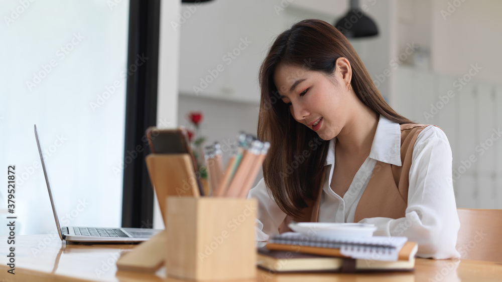 Female college student doing assignment with digital devices and stationery