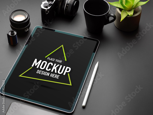 Black table with mock up tablet, camera, mug, plant pot and copy space