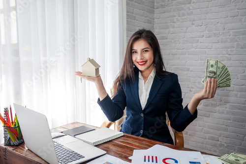 Beautiful asian businesswoman holding dollar bills and a house model. Home and land trading concept. photo