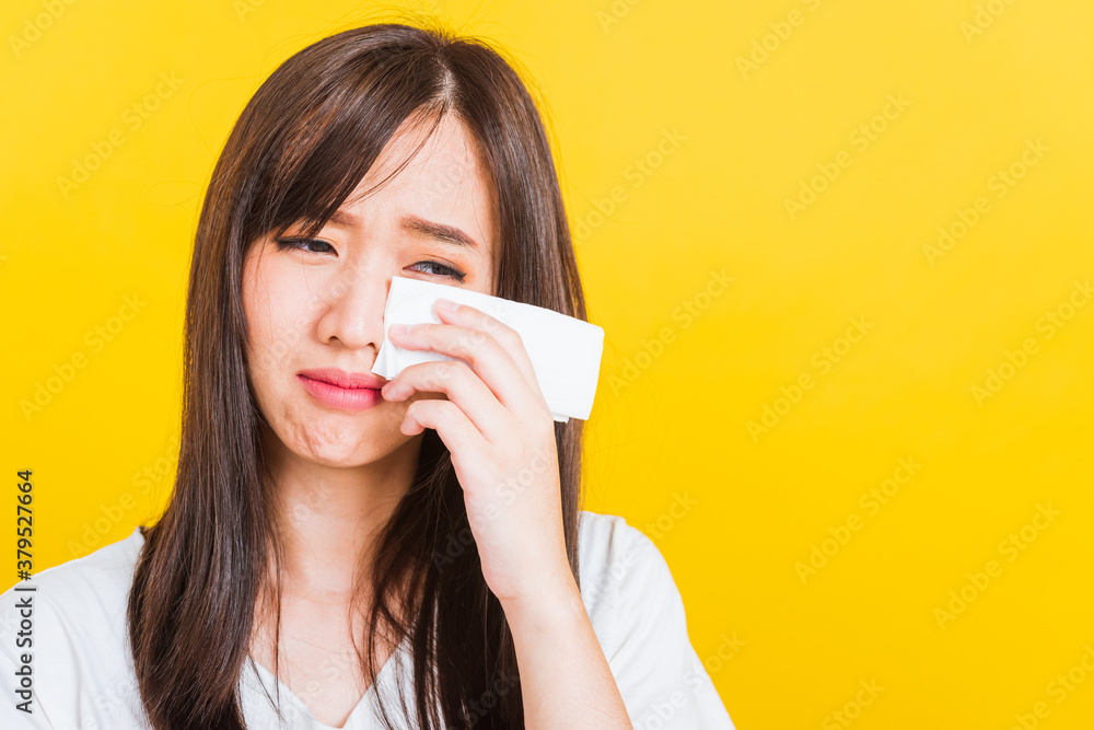 Portrait of Asian beautiful young woman sad she crying wiping tears from eyes with a tissue, Close up of pretty girl feeling depressed upset unhappy, studio shot isolated on yellow background Portrait of Asian beautiful young woman sad she crying wiping tears from eyes with a tissue, Close up of pretty girl feeling depressed upset unhappy, studio shot isolated on yellow background