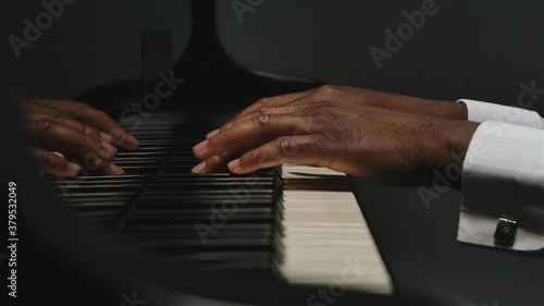 Footage of male hands playing the grand piano. An African American man touches his fingers on the black and white keys. The pianist plays the beautiful grand piano in slow motion. Close up.