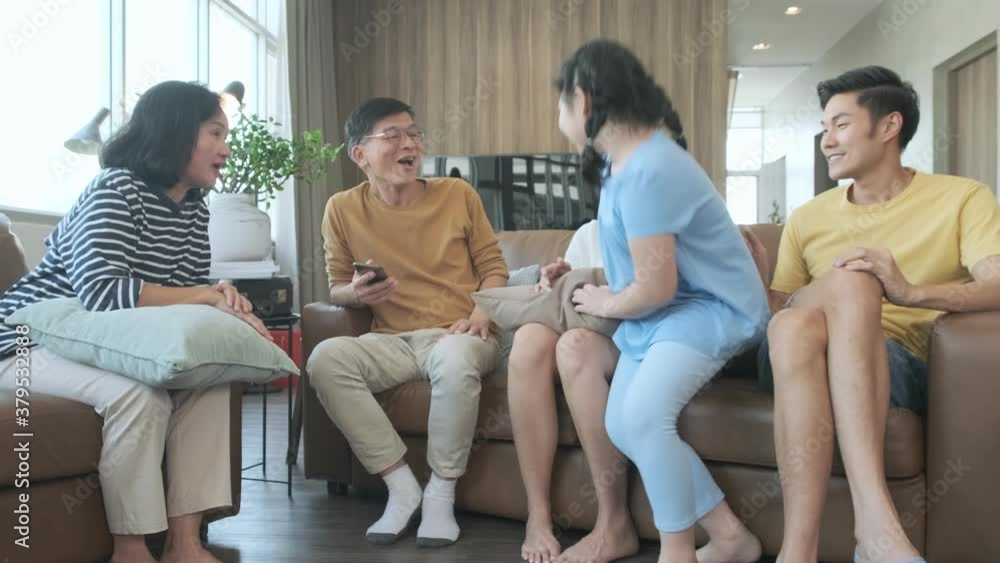 Asian happy big family smiling and watching conversation together in cozy room. Joyful man and woman sitting on sofa with kid daughter and parents. Grandparents, parents and children running around
