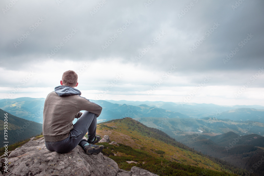 young strong man sitting on the rock at the top of the mountains peak young strong man sitting on the rock at the top of the mountains peak