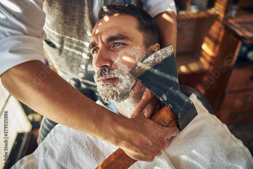 Handsome young man being shaved with an axe