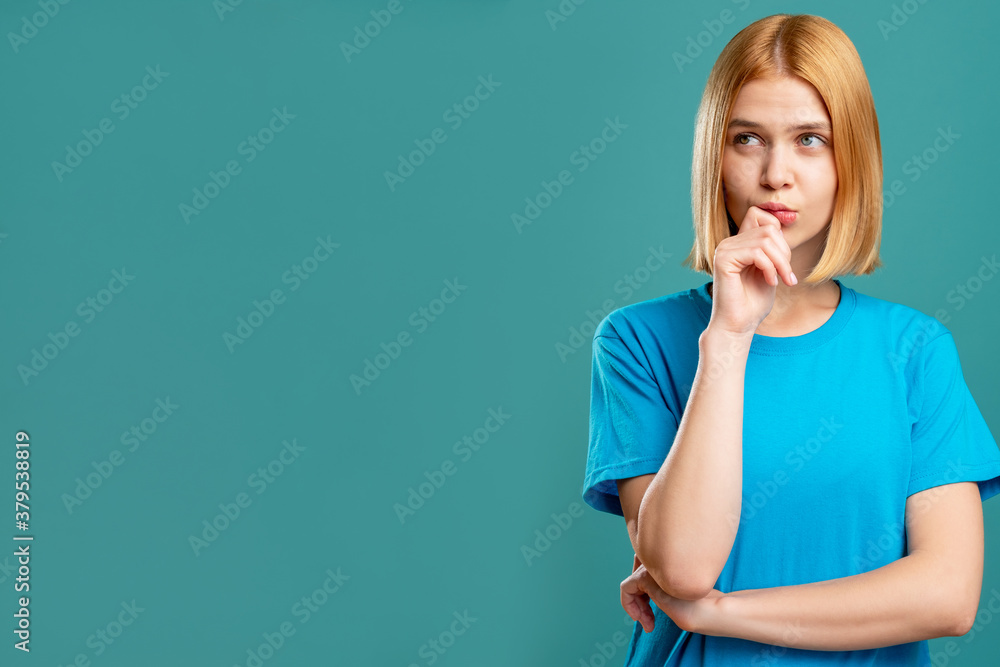 Doubtful woman. Problem solution. Portrait of pensive blonde lady in blue t-shirt looking at copy space isolated on teal promotional background. Special offer. Motivation discovery. Doubtful woman. Problem solution. Portrait of pensive blonde lady in blue t-shirt looking at copy space isolated on teal promotional background. Special offer. Motivation discovery.