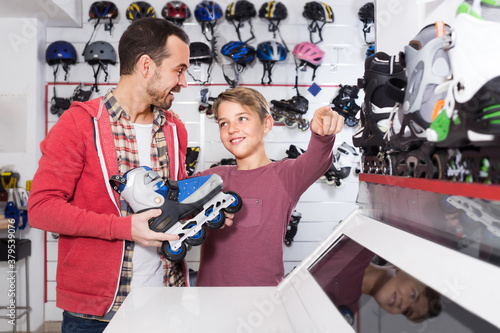 Man 30s years old with his son 10s years old choosing new roller-skates in sports store.