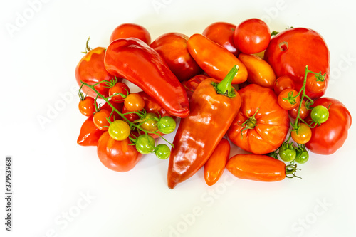 Collection of fresh red tomatoes and peppers from above on white plate with copy space