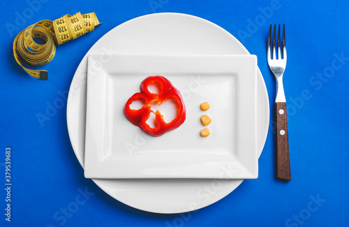 Plate with vegetables, fork and measuring tape on color background. Concept of anorexia