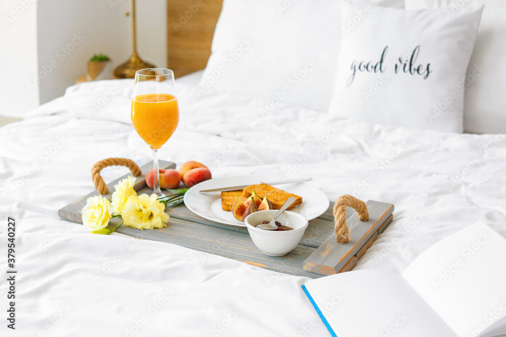 Tray with tasty breakfast and book on bed