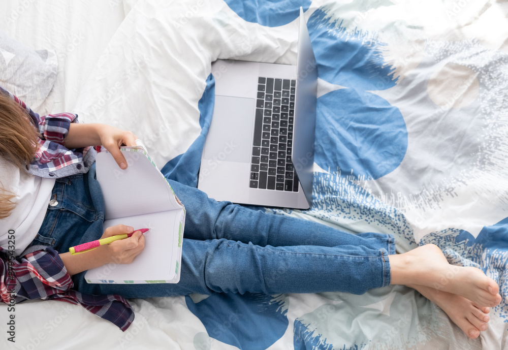 Fototapeta premium Distance learning online education. Schoolgirl studying at home with digital laptop notebook and doing school homework lying on bed at home.