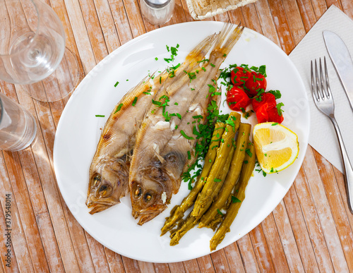 Whole oven baked rooster fish with marinated asparagus and tomatoes on white plate photo