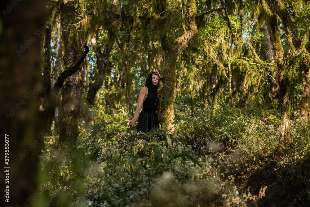 Girl in a black hood dress walking through the woods, enjoying the walk fashion. Anxious tired, worth, brooding, dreamy in green forest, trees, path. Enjoying the walk. Magic. High quality photo