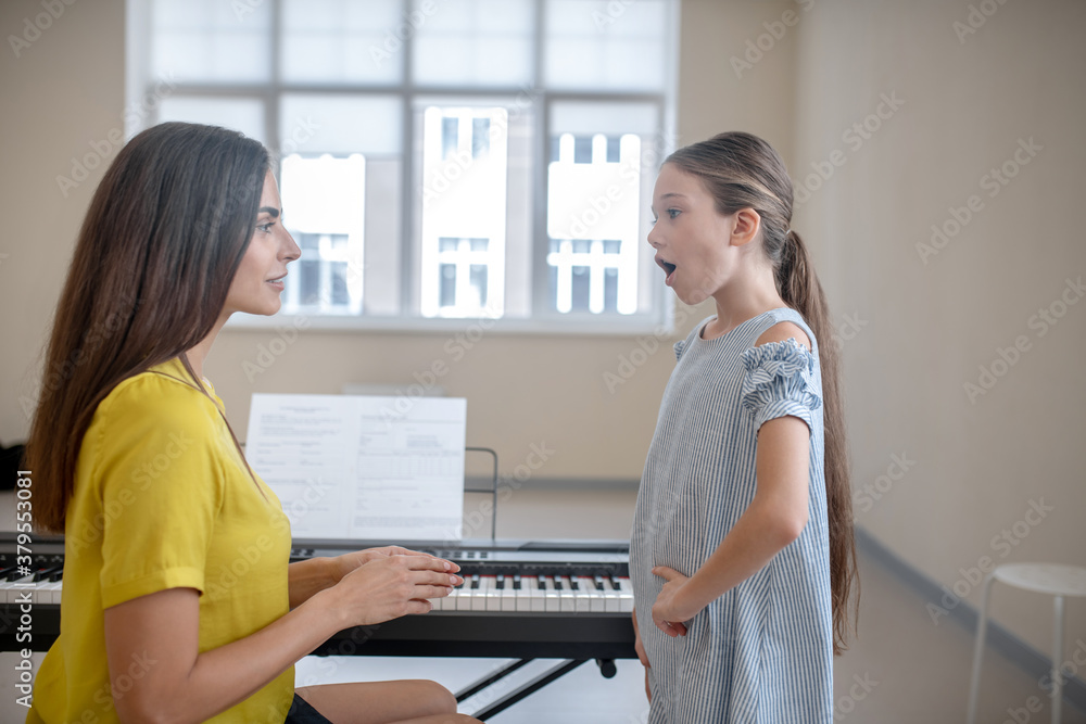 Obraz premium Girl in a blue dress having a vocal lesson
