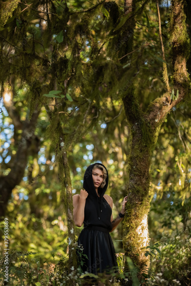 Girl in a black hood dress walking through the woods, enjoying the walk fashion. Anxious tired, worth, brooding, dreamy in green forest, trees, path. Enjoying the walk. Magic. High quality photo Girl in a black hood dress walking through the woods, enjoying the walk fashion. Anxious tired, worth, brooding, dreamy in green forest, trees, path. Enjoying the walk. Magic. High quality photo