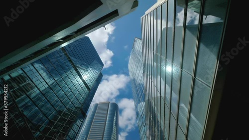 Timelpase of low angle view of city skyline buildings, blue sky and glass mirrored facades.