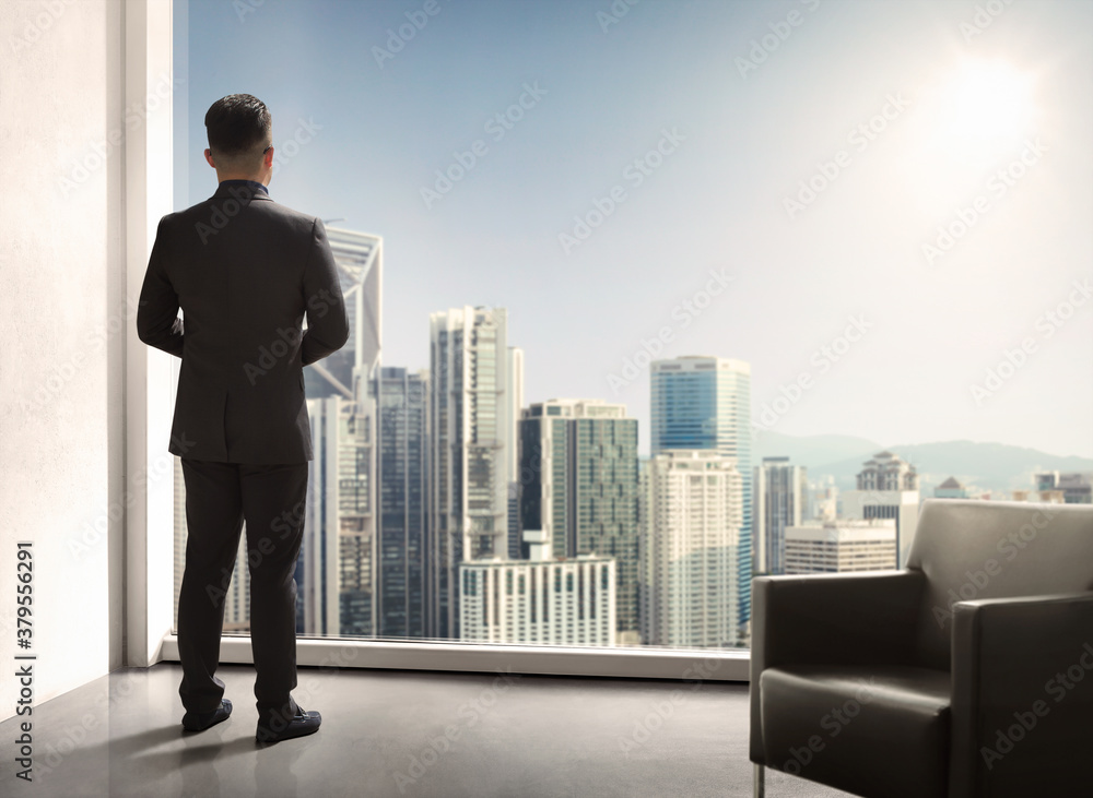 Young businessman standing in front full-length window looking at cityscape with skyscrapers, inspiration or enjoying, waiting for meeting or considering business offer Young businessman standing in front full-length window looking at cityscape with skyscrapers, inspiration or enjoying, waiting for meeting or considering business offer