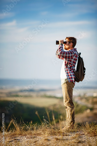 Konstfotografi Guy looking at binoculars in hill. man in t-shirt with backpack.