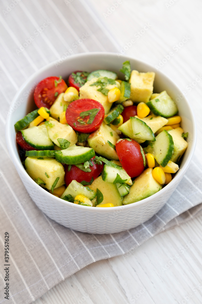 Fresh Avocado Tomato Salad in a bowl on a white wooden background, low angle view.