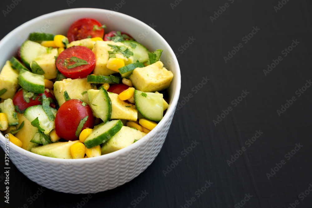 Fresh Avocado Tomato Salad in a bowl on a black surface, side view. Copy space.