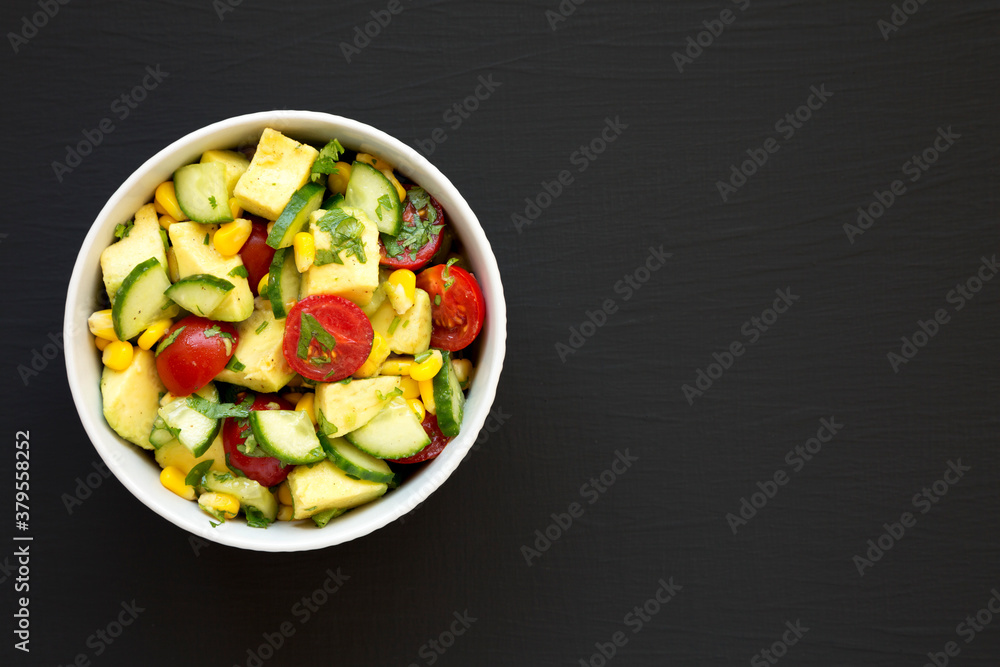 Fresh Avocado Tomato Salad in a bowl on a black surface, top view. Flat lay, overhead, from above. Space for text.